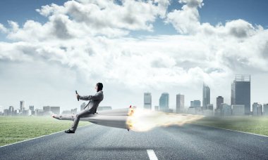 Cityscape ve mavi gökyüzü arka plan üzerinde ile roket yukarıda asfalt yol üzerinde uçan takım elbiseli genç işadamı kavramsal görüntü.