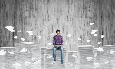 Arka plan gri duvar ile kağıt uçan arasında casual giyim oturan genç adam uçakları. Karışık teknik.