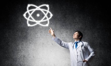 Başarılı ve beyaz üniformalı genç bir doktor, arka planda gri beton duvara karşı dururken moleküler yapıyla etkileşime giriyor..