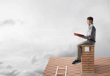 Elinde kırmızı kitap ile evin baca rahat oturan genç adam