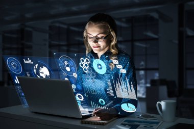 Çekici bir kadın gece ofisinde oturmuş dizüstü bilgisayarına bakıyor. Karışık ortam