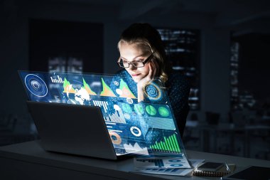 Çekici bir kadın gece ofisinde oturmuş dizüstü bilgisayarına bakıyor. Karışık ortam