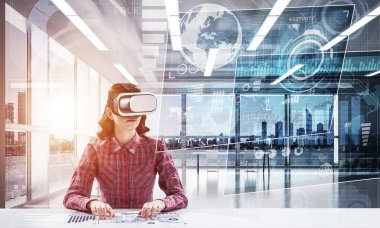 Parlak ofis binasında otururken dijital medya arayüzü olan VR kulaklık kullanan kareli gömlekli genç bir kadın. Eğitim için sanal gerçeklik teknolojileri