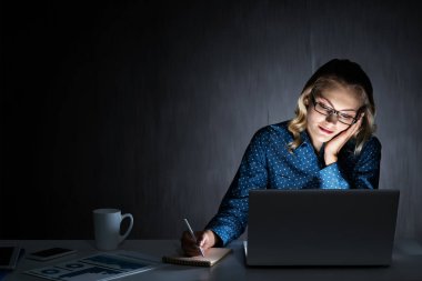 Genç bir kadın gece geç saatlerde odasında ya da ofisinde oturuyor. Karışık ortam