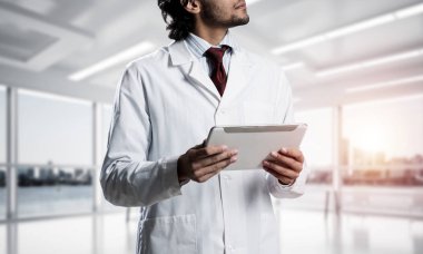 Beyaz steril önlük ayakta beyaz hastane ofis güneş ışığı ile arka plan üzerinde binası içinde kendine güvenen doktor görüntü kırpılmış.