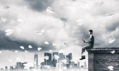 Elinde cep telefonu ile üst yapı üzerinde oturan genç işadamı