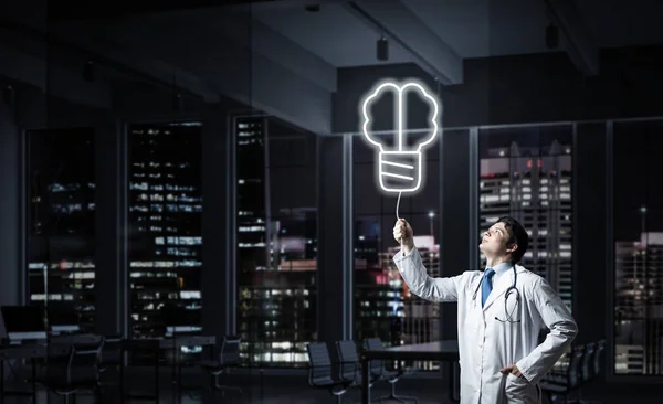 Professional medical industry employee in white medical suit interracting with glowing screw symbol in the air while standing against night cityscape view on background.