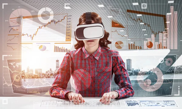 Educational process with help of VR headset. Cheerful young woman in checkered shirt using digital media interface while sitting indoors of office building.