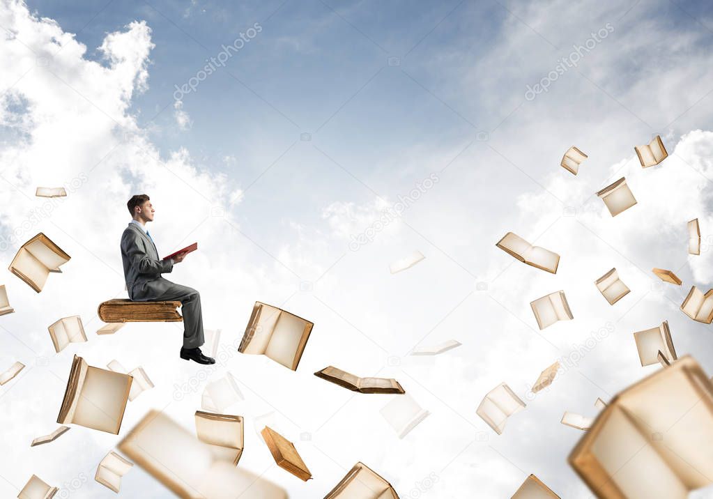 Young businessman floating in blue sky with red book in hands