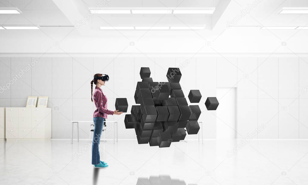 Young woman in casual wearing virtual helmet and looking at cube figure. 3d rendering