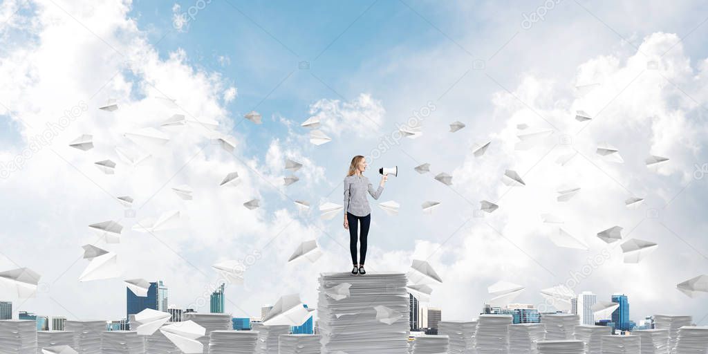 Woman in casual clothing standing among flying paper planes with speaker in hand and with skyscape on background. Mixed media.
