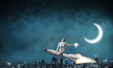 Arka plan üzerinde gece cityscape ve mavi gökyüzü ile roket üzerinde uçan takım elbiseli genç işadamı kavramsal görüntü.