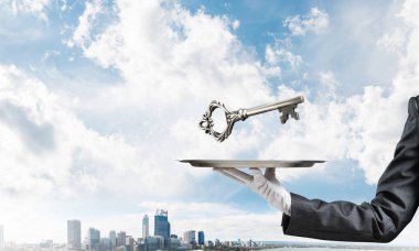 Büyük anahtar arka plan üzerinde cityscape manzaralı metal tepside sunan beyaz eldivenli elinde garsonun kırpılmış görüntü.