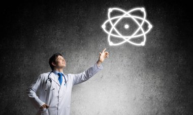Başarılı ve beyaz üniformalı genç bir doktor, arka planda gri beton duvara karşı dururken moleküler yapıyla etkileşime giriyor..