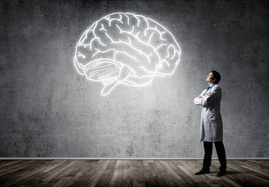 Beyaz Tıbbi üniforma silah tutmak ve arka planda gri duvara ayakta iken parlayan beyin sembolü bakarak Genç ve emin doktor.