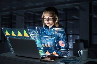 Çekici bir kadın gece ofisinde oturmuş dizüstü bilgisayarına bakıyor. Karışık ortam