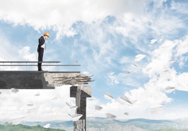 Genç takım elbiseli mühendis ve arka plan üzerinde hava ve Doğa Manzaralı kırık köprüde kağıt uçak uçan arasında duran bakıyordu kask. 3D render.