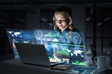 Çekici bir kadın gece ofisinde oturmuş dizüstü bilgisayarına bakıyor. Karışık ortam