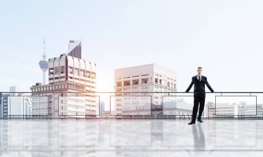 Balkonda takım elbiseli genç bir işadamı sabah şehir manzarasına karşı.