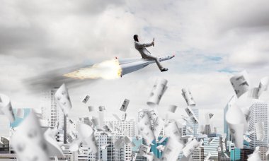 Kağıtları ile modern cityscape gökdelenler ve mavi gökyüzü ile arka plan üzerinde uçan arasında roket üzerinde uçan takım elbiseli Genç ve mutlu işadamı kavramsal görüntü.