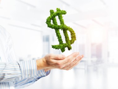 Dolar işareti tutan erkek el kapanışını yeşil otların yaptı. Karışık teknik
