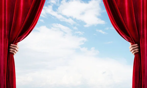 人間の手は青い空を背景に赤いベルベットのカーテンを開きます — ストック写真