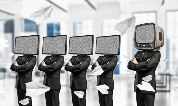 Businessmen in suits with TV instead of their heads keeping arms crossed while standing in a row and one at the head with old TV inside office building.