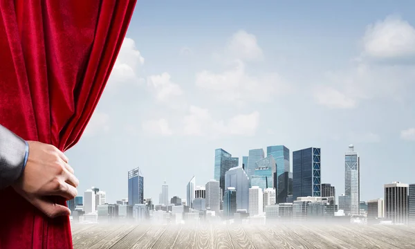 人間の手は近代的な都市景観と曇り空に赤いベルベットのカーテンを開きます — ストック写真