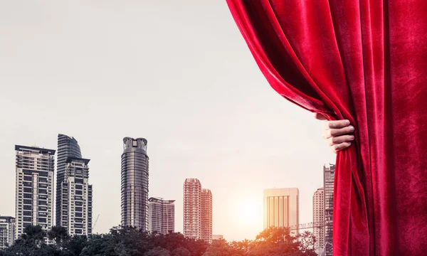 赤いベルベットのカーテンと背景に街並みを開く実業家の手 — ストック写真
