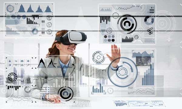 Horizontal shot of young successful business woman sitting inside office and using virtual reality headset with digital media interface