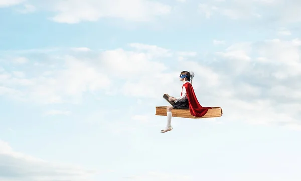 空に本の上に浮かぶマスクとケープの小さな子供と読書 — ストック写真