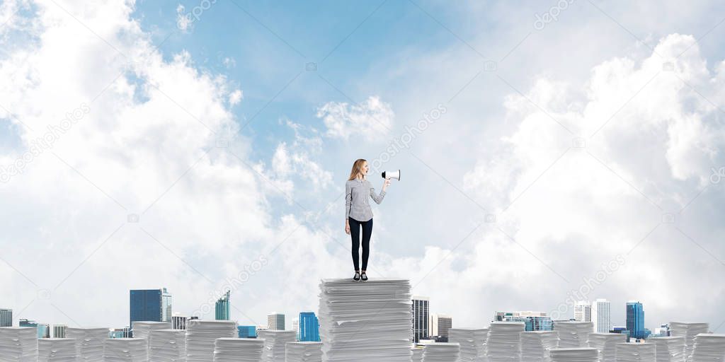 Woman in casual clothing standing on pile of documents with speaker in hand with skyscape and city view on background. Mixed media.