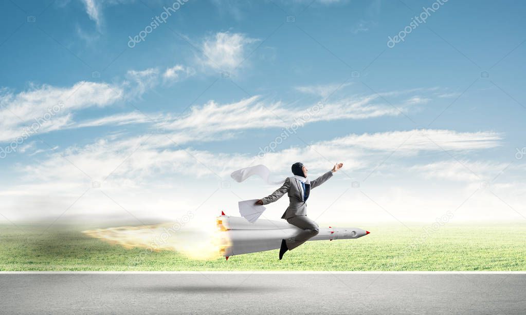 Conceptual image of young businessman in suit flying on rocket above asphalt road with blue cloudy sky on background.