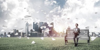 Kırmızı gözlüklü ve takım elbiseli komik adam bankta oturup kitap okuyor.