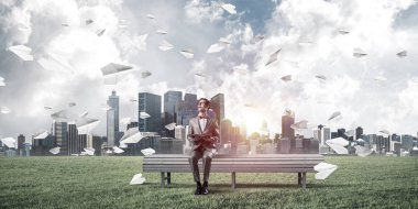 Kırmızı gözlüklü ve takım elbiseli komik adam bankta oturup kitap okuyor.