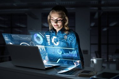 Çekici bir kadın gece ofisinde oturmuş dizüstü bilgisayarına bakıyor. Karışık ortam