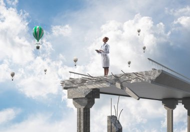 Peyzaj görünümü ve arka planda uçan hava balonları ile kırık köprünün kenarında ayakta iken tablet telefon kullanan profesyonel kadın doktor. Medikal Sanayi konsepti