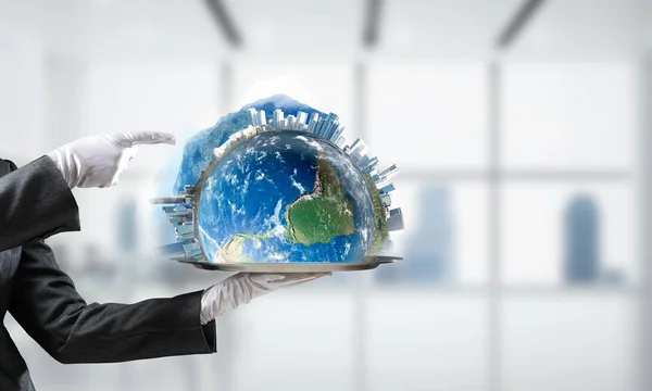 Cropped image of waitress\'s hand in white glove presenting Earth globe on metal tray and pointing on it with office view on background. 3D rendering. Elements of this image are furnished by NASA.