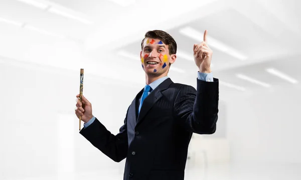 黒のスーツを手に絵筆を保持し ながら近代的な明るいオフィス中に立って笑顔で若くて成功した実業家の概念図 — ストック写真