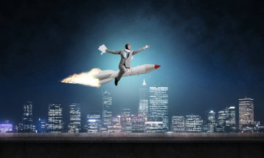 Arka plan üzerinde gece cityscape ve mavi gökyüzü ile roket üzerinde uçan takım elbiseli genç işadamı kavramsal görüntü.