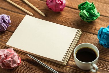 Not defteri, kalemler, buruşmuş kağıt toplar ve ahşap masa üzerinde kahve olan modern yaratıcı işyerinin düşük açılı görüntüsü..