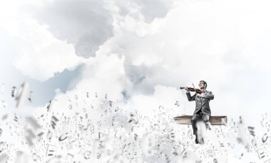 Takım elbiseli ve gözlüklü genç adam kitaba oturup keman çalıyor.