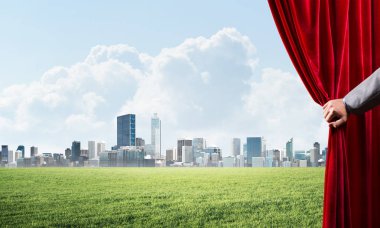 İnsan eli kırmızı kadife perde cityscape ve yeşil çayır açar