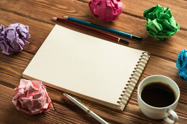 Not defteri, kalemler, buruşmuş kağıt toplar ve ahşap masa üzerinde kahve olan modern yaratıcı işyerinin düşük açılı görüntüsü..
