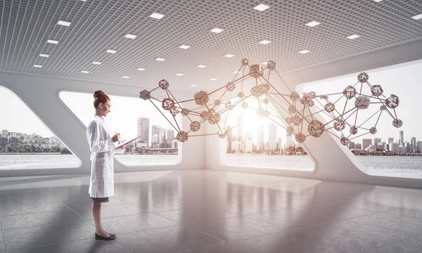 Young woman doctor in white medical suit studying social network structure while standing inside white hospital building. Medical industry concept