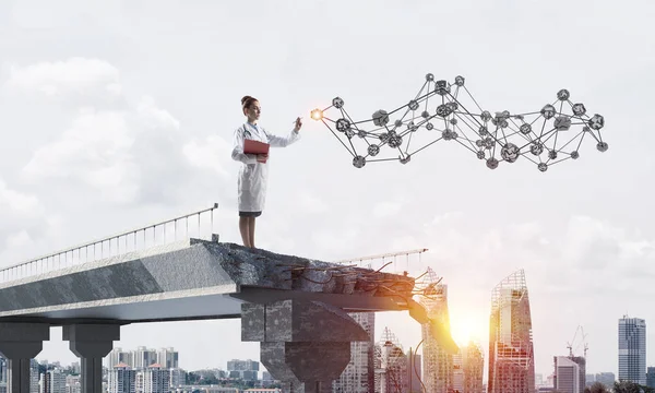 Young medical industry employee in white medical uniform with social network structure while standing at the end of broken bridge. Medical industry concept. Cityscape view on background