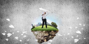 Takım elbiseli genç işadamının uçan kağıt uçakların arasında elinde büyük beyaz bir okla uçan adada dikilirken ve arka planda koyu gri bir duvara yaslanırken kavramsal görüntüsü..