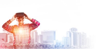 Sanal gerçeklik kulaklığı olan genç bir adam ya da şehrin arka planında 3 boyutlu gözlüklü.