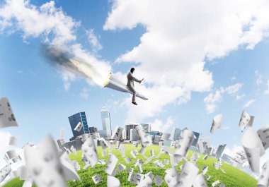Kağıtları cityscape ve mavi gökyüzü ile arka plan üzerinde uçan arasında roket üzerinde uçan takım elbiseli genç işadamı kavramsal görüntü.