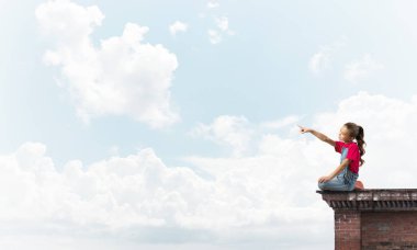 Üstte oturan ve bir şeyi işaret eden sevimli bir kız.